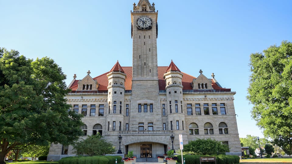 A large, historic building with a clock tower, surrounded by well-maintained lawns and trees.