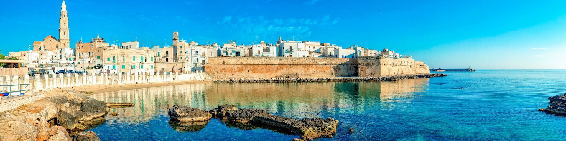 Una ciudad costera con edificios históricos, una torre destacada y aguas azules cristalinas.