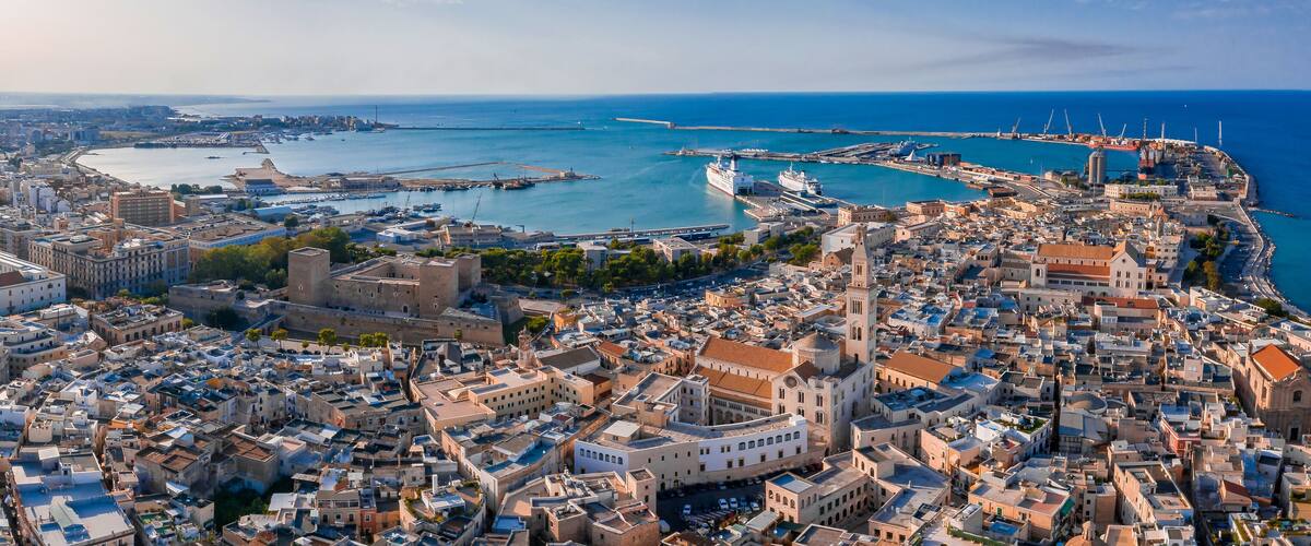 A coastal cityscape with dense urban architecture, a prominent port with ships, and a historic fortress.