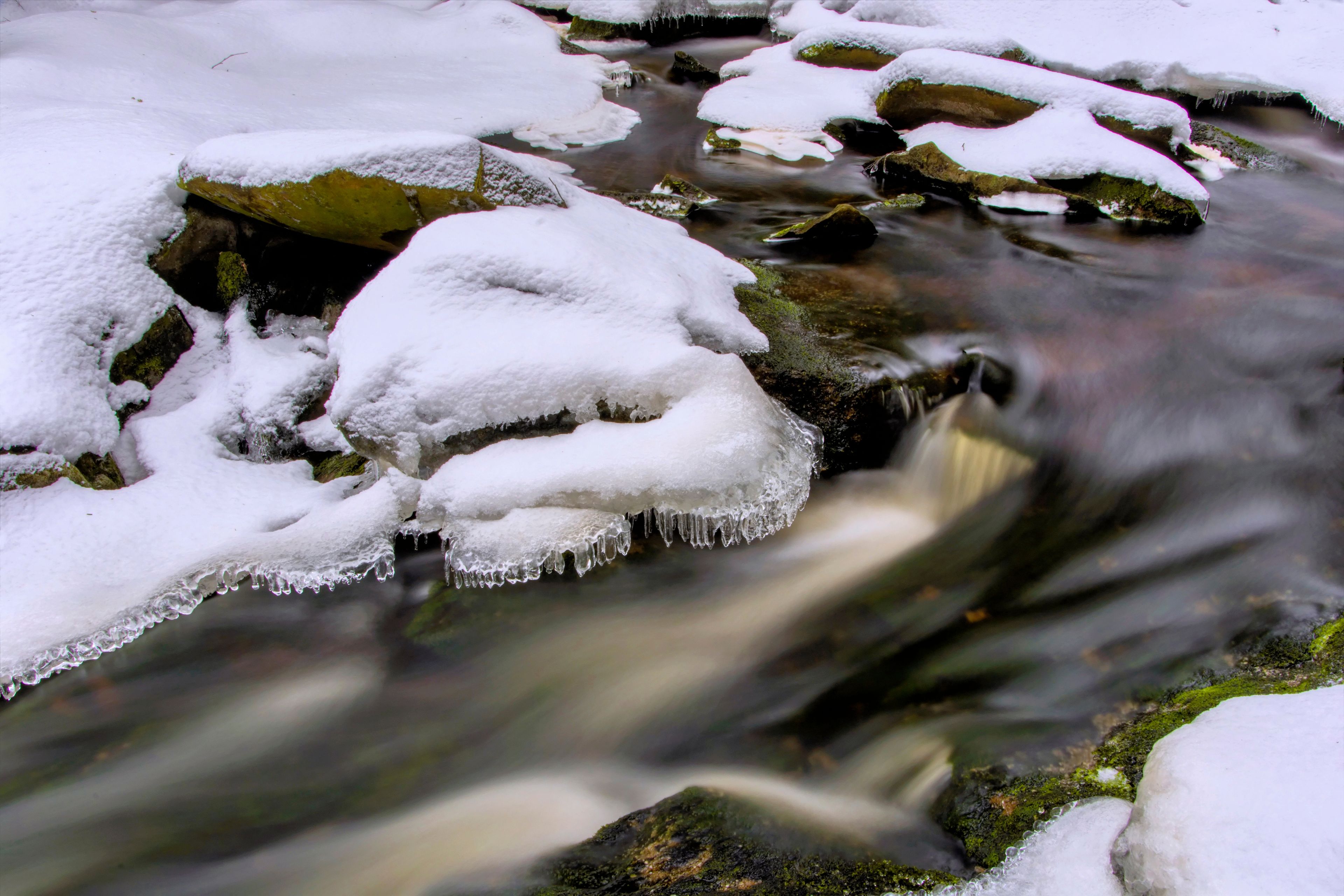 A snow-covered stream with icicles hanging from rocks.