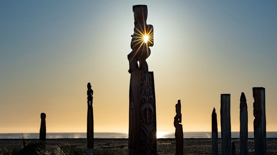 A series of stone sculptures at sunset with the sun shining through one.