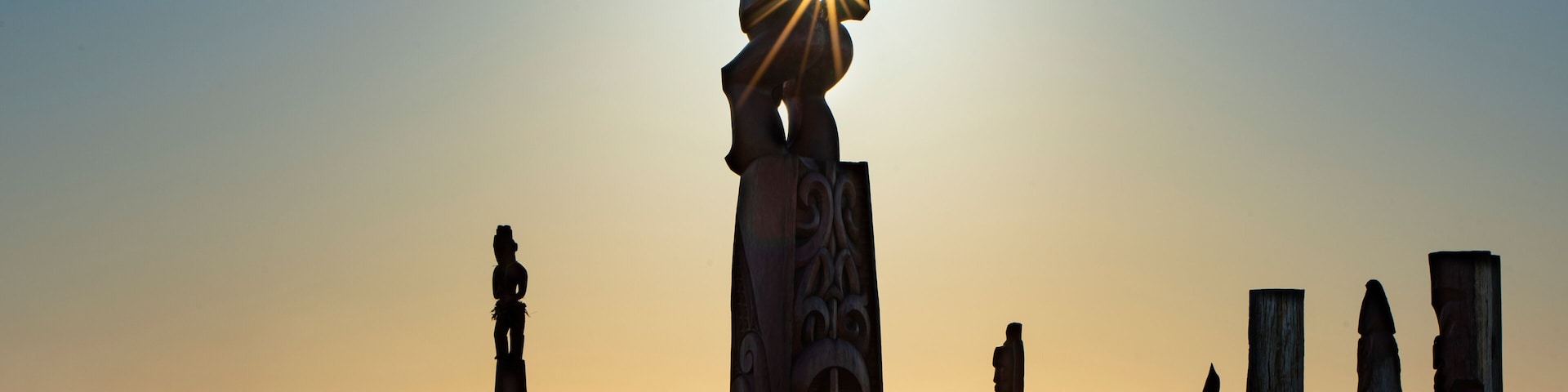 A series of stone sculptures at sunset with the sun shining through one.