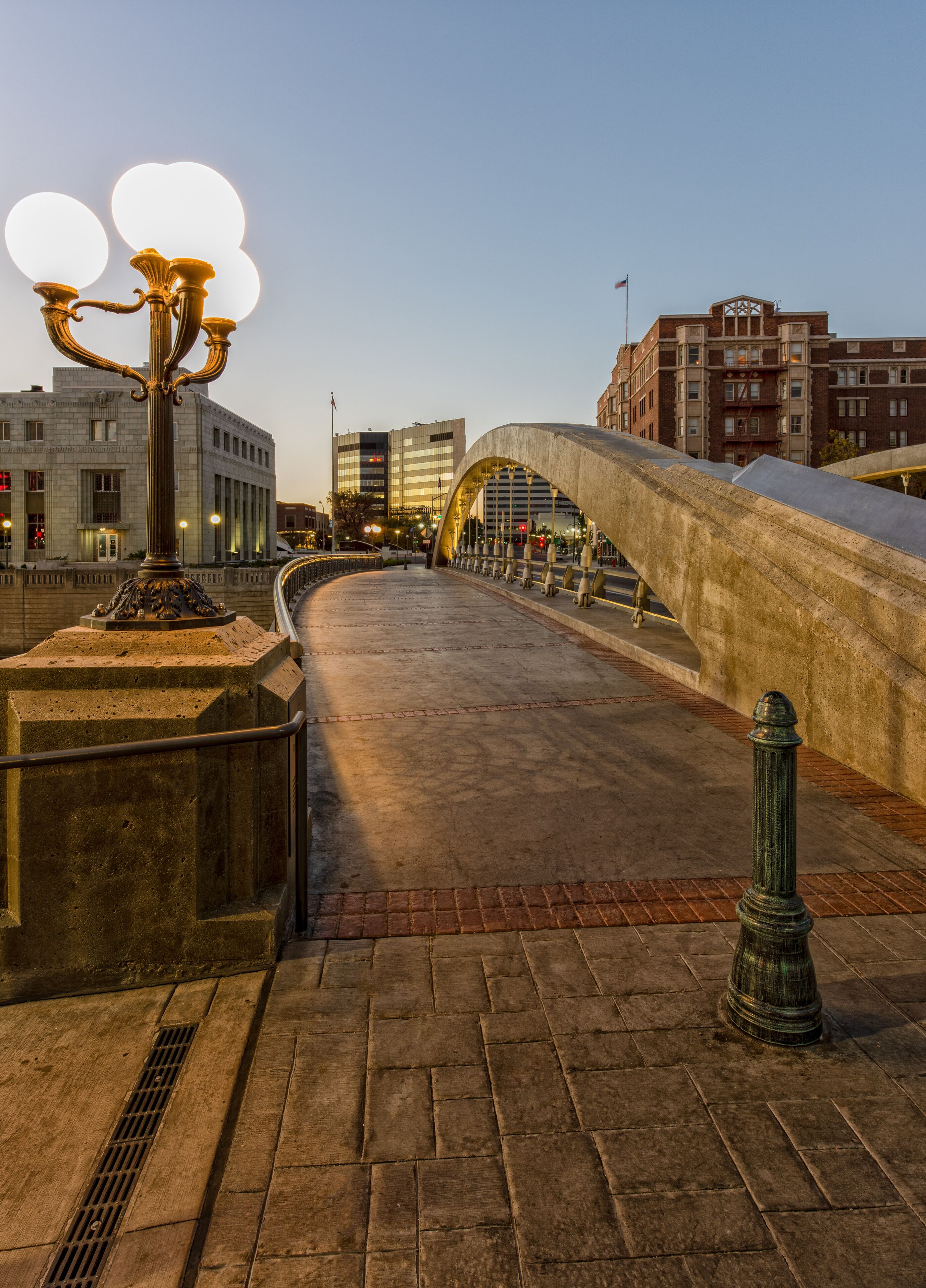 Uma ponte com arco curvo, um poste de luz e edifícios ao fundo.