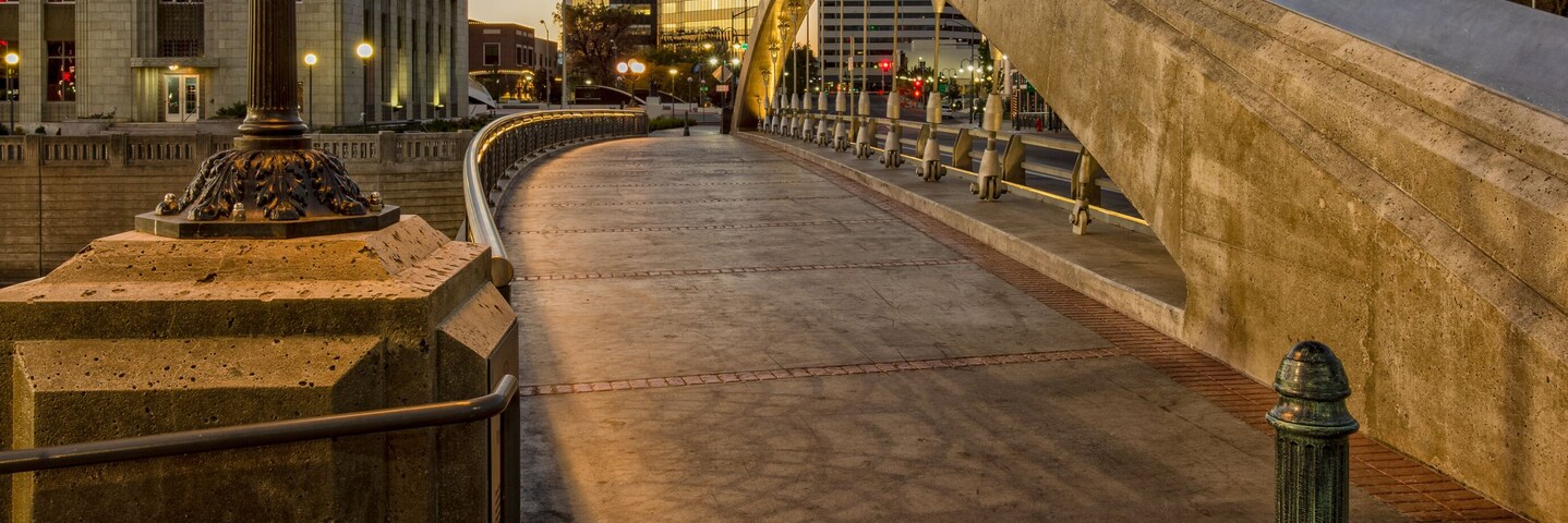 Uma ponte com arco curvo, um poste de luz e edifícios ao fundo.