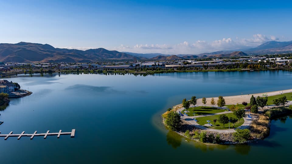 A calm lake with a dock, a park with a gazebo, and mountains in the background.