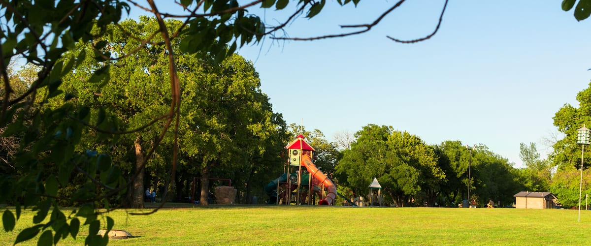 A playground with a slide and climbing structures, surrounded by trees and grass.