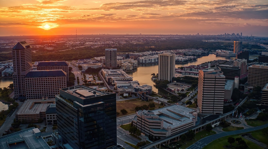 A cityscape at sunset with a river, high-rise buildings, and a bridge.
