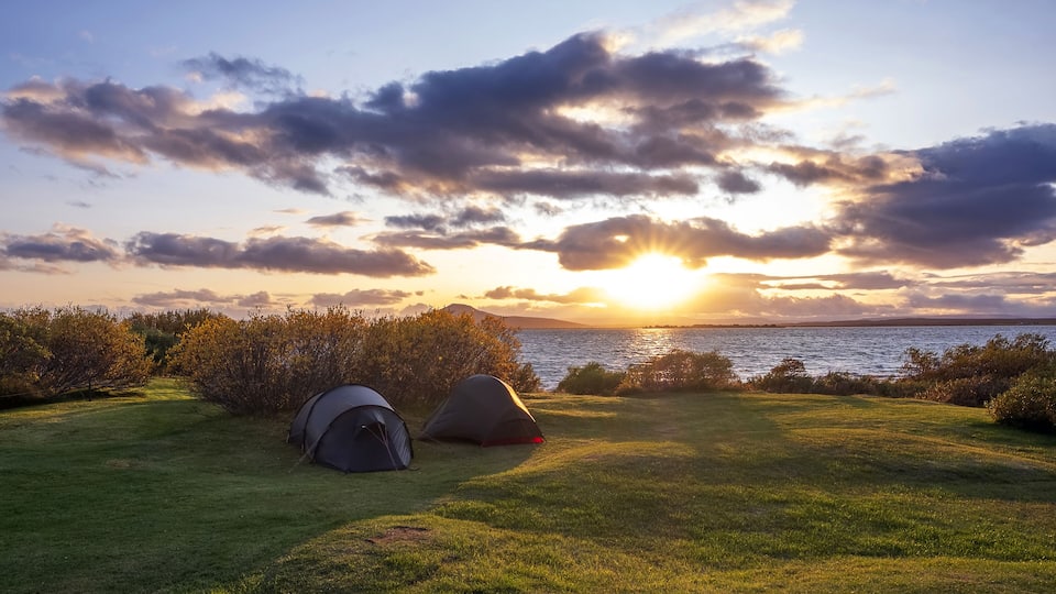 A sunset over a body of water with two tents on a grassy field.