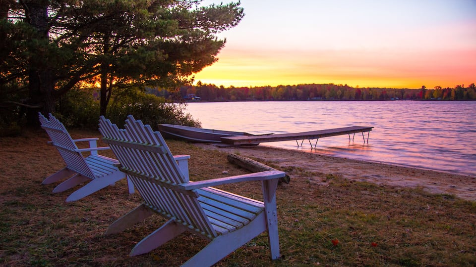 A lakeside scene with Adirondack chairs and a dock extending into the water.