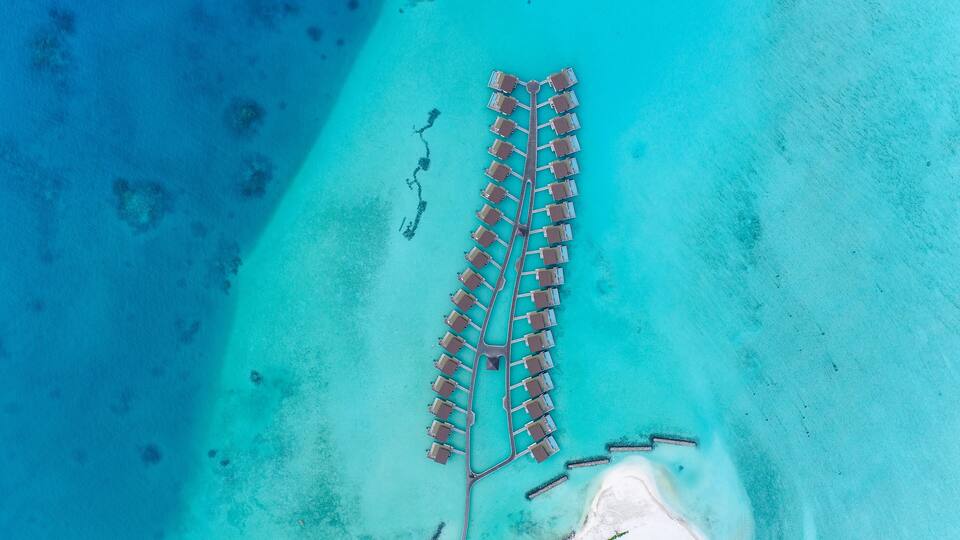 An aerial view of a resort with a long pier extending into turquoise waters, surrounded by clear skies.