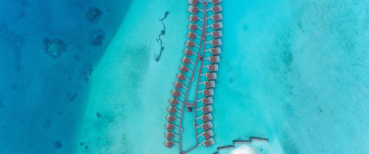 An aerial view of a resort with a long pier extending into turquoise waters, surrounded by clear skies.
