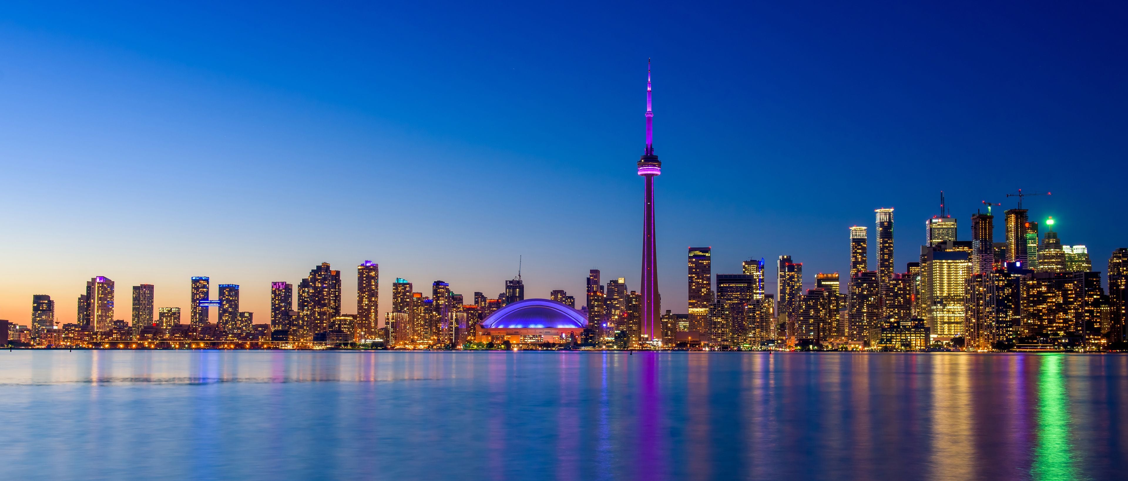 A city skyline at dusk with illuminated buildings and a prominent tower.