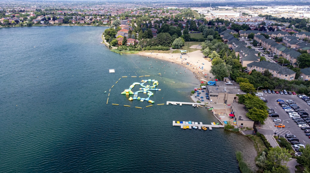 Un lago con un varco per barche, una spiaggia sabbiosa e una zona residenziale con auto parcheggiate.