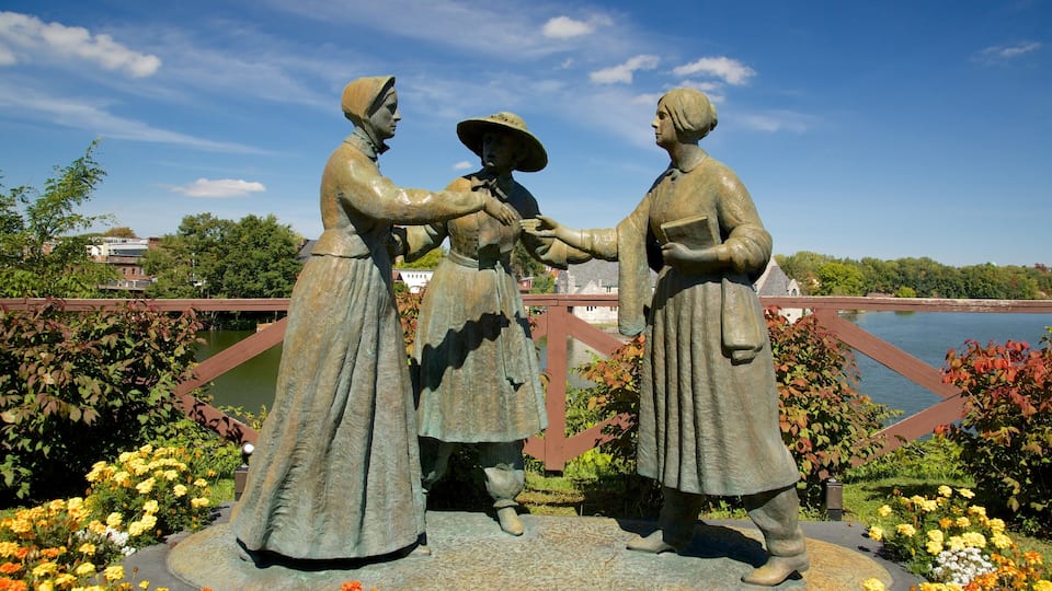 A bronze statue of three figures in traditional attire, surrounded by vibrant flowers and a bridge in the background.