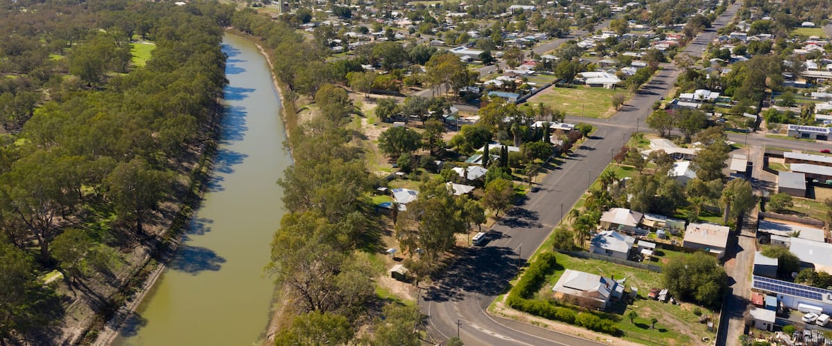 An aerial view of a riverside town with houses, a river, and surrounding greenery.