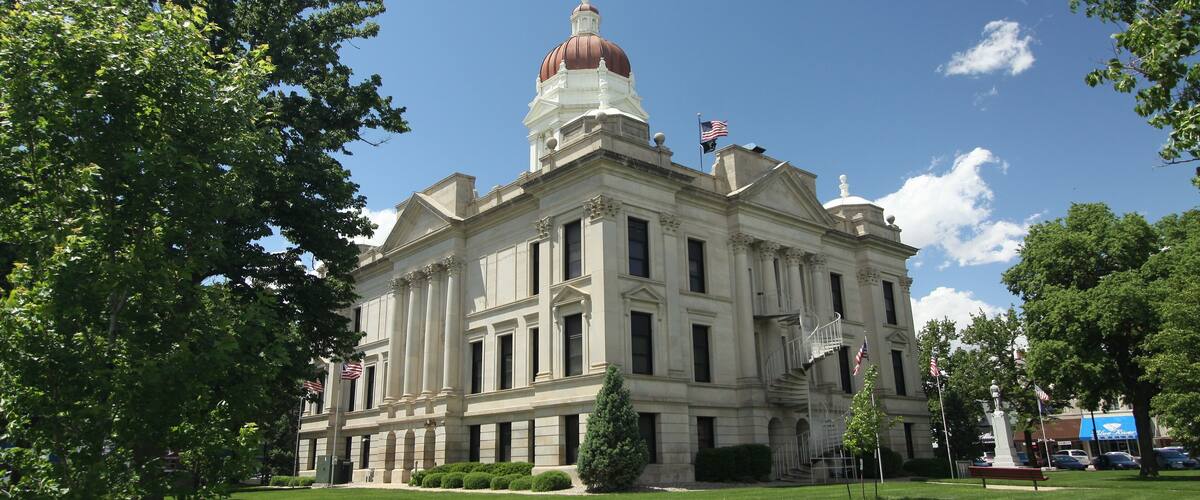 A large, historic building with a prominent dome and columns, surrounded by well-maintained lawns and trees.