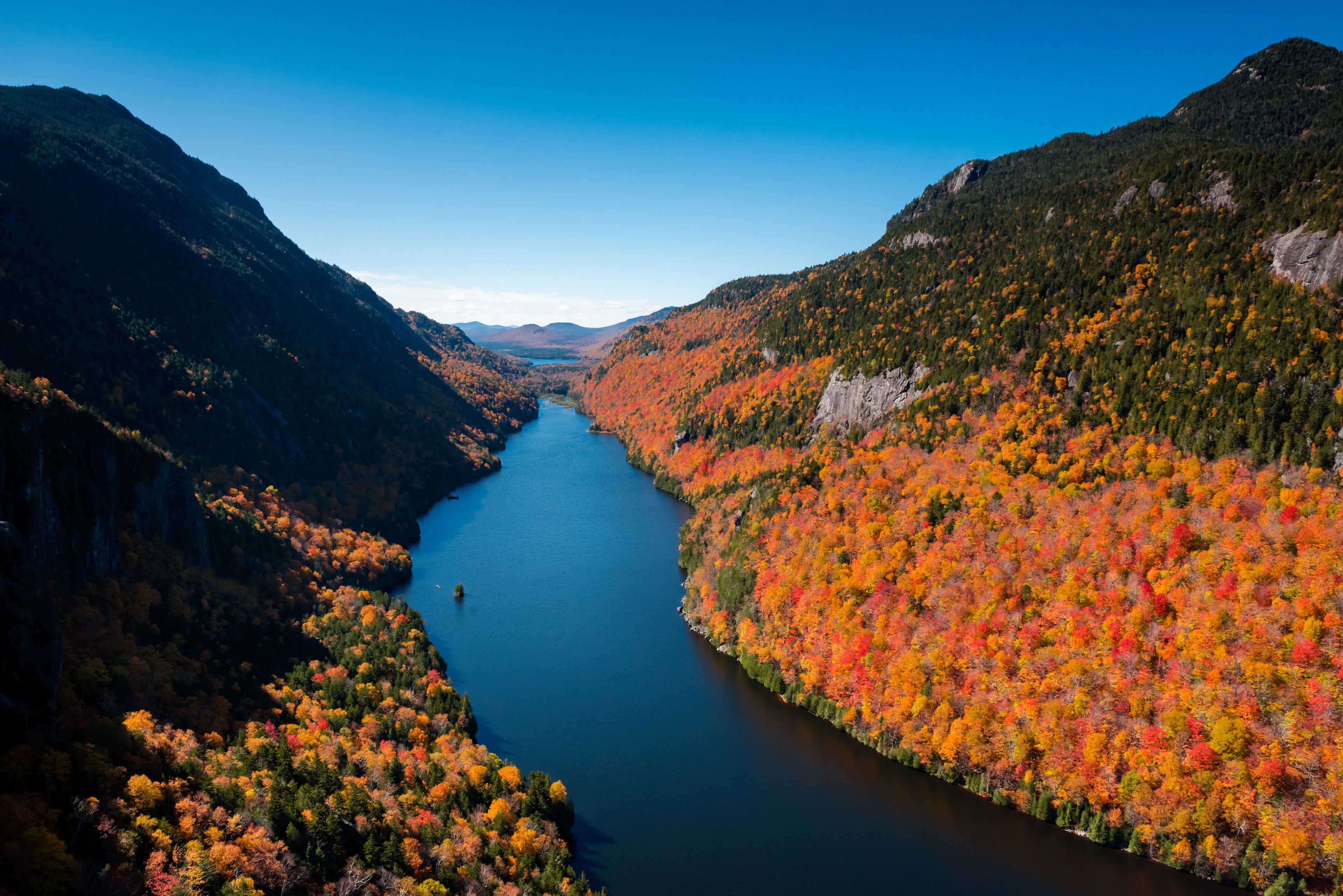 A river flanked by mountains with autumn foliage.