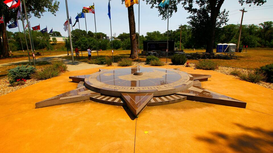 A circular monument with a compass design and the words "Geographic Union" on it, surrounded by a paved area with flags and trees.