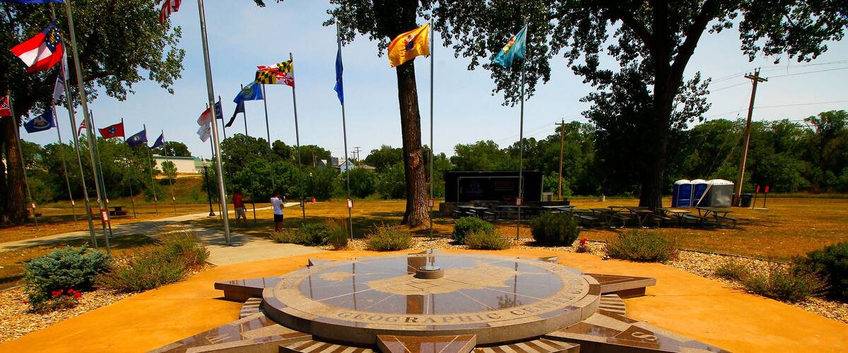 A circular monument with a compass design and the words "Geographic Union" on it, surrounded by a paved area with flags and trees.