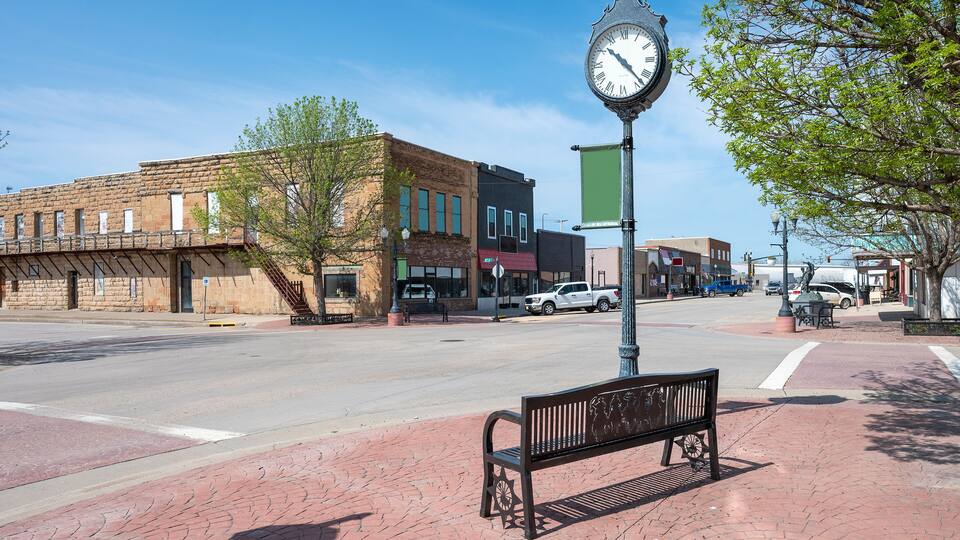 A street with a clock, a bench, and buildings.