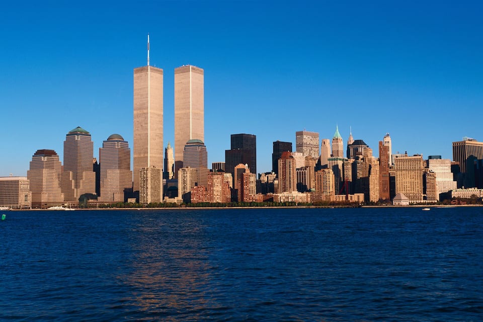 A city skyline with prominent twin towers, a variety of skyscrapers, and a body of water in the foreground.