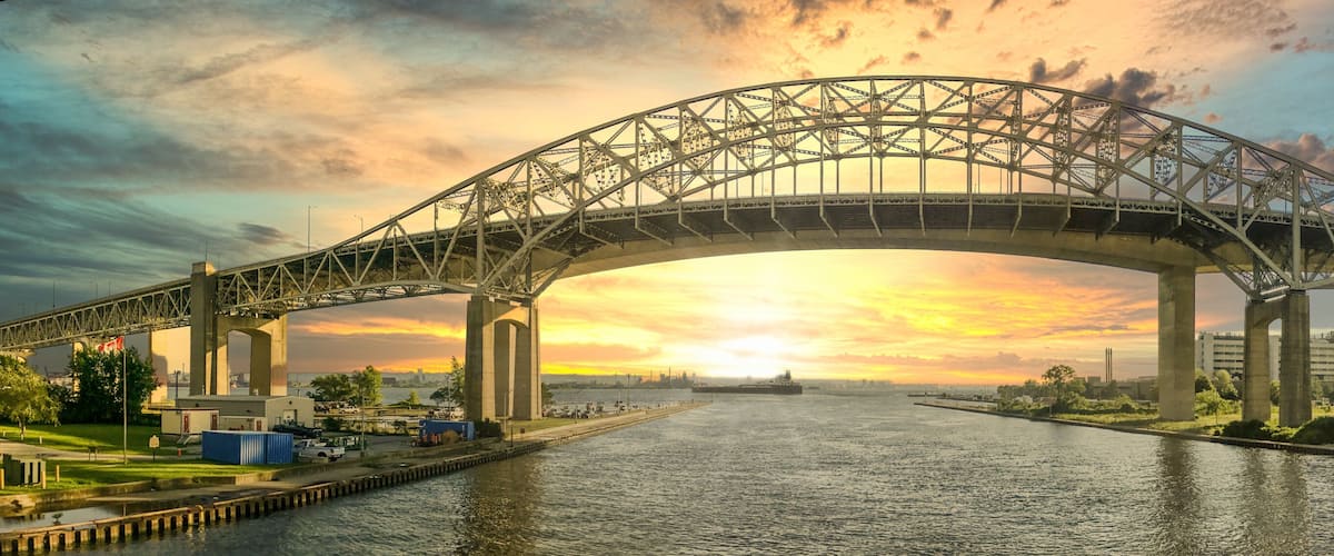 Un gran puente de acero que cruza un río, con un atardecer de fondo.
