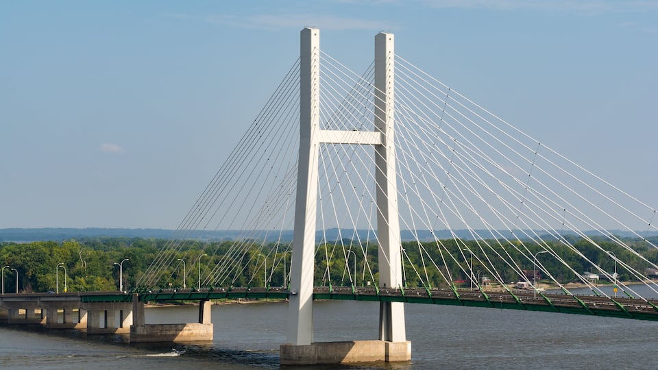 A large white cable-stayed bridge over a river with green supports and a forested landscape in the background.