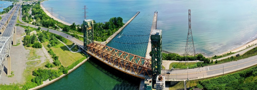 Un gran puente de acero que cruza un río, con una playa y carreteras a ambos lados.
