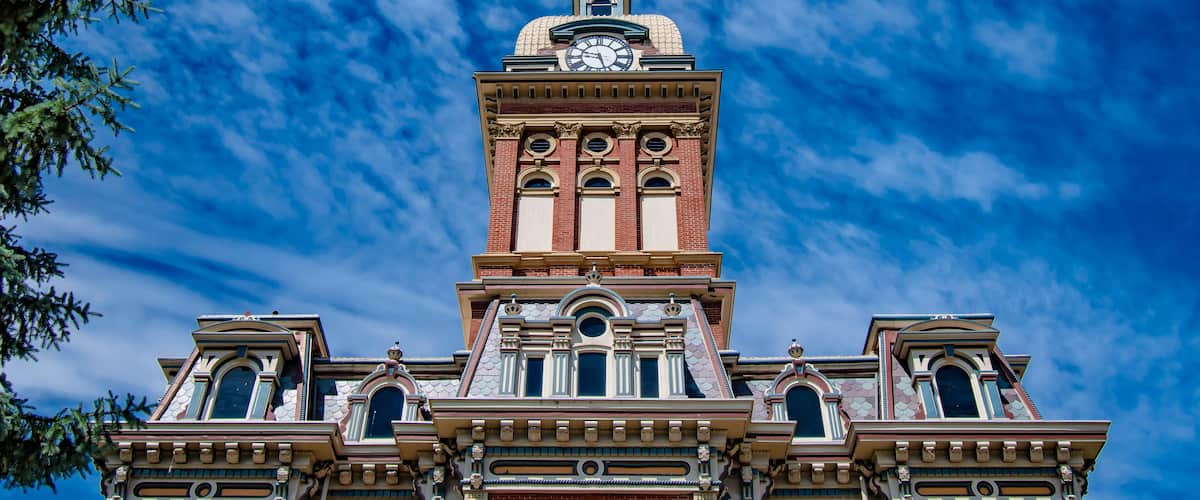 A historic building with a clock tower, arched windows, and intricate architectural details against a blue sky with clouds.