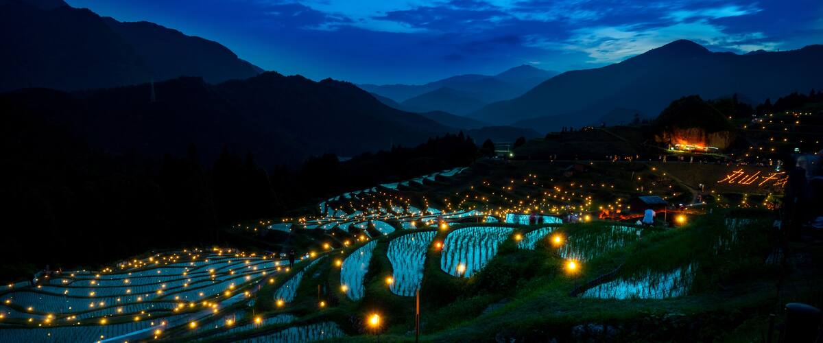 Terraced rice fields at dusk with lights illuminating the landscape.