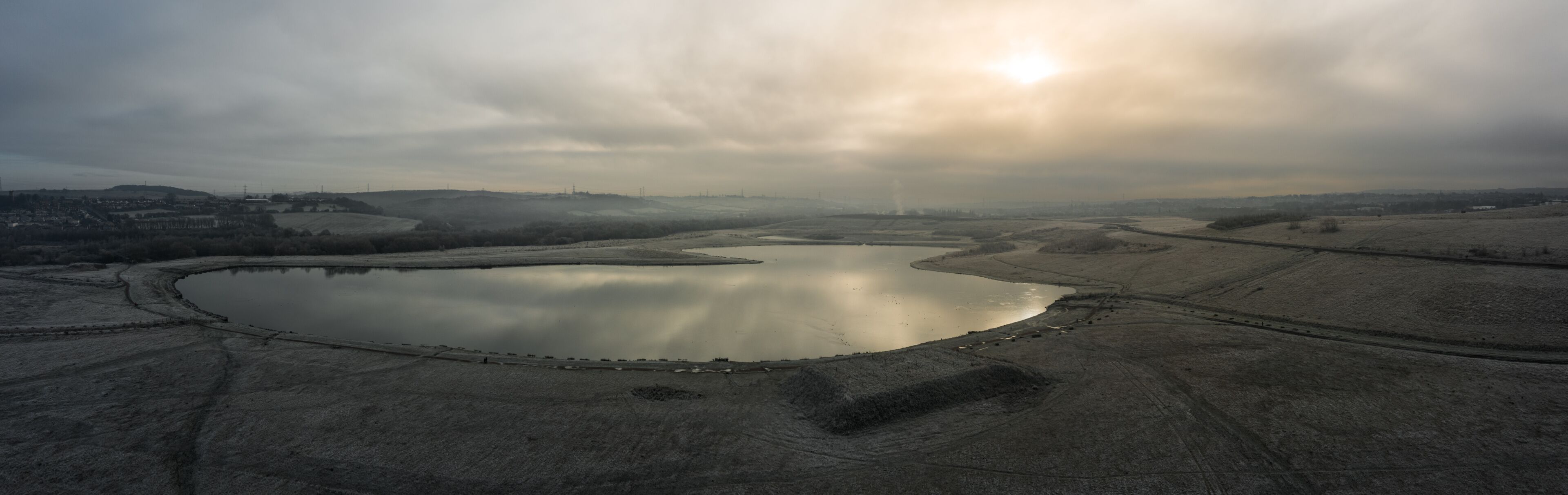 Una extensa masa de agua rodeada de terreno árido, con colinas distantes y un cielo nublado.
