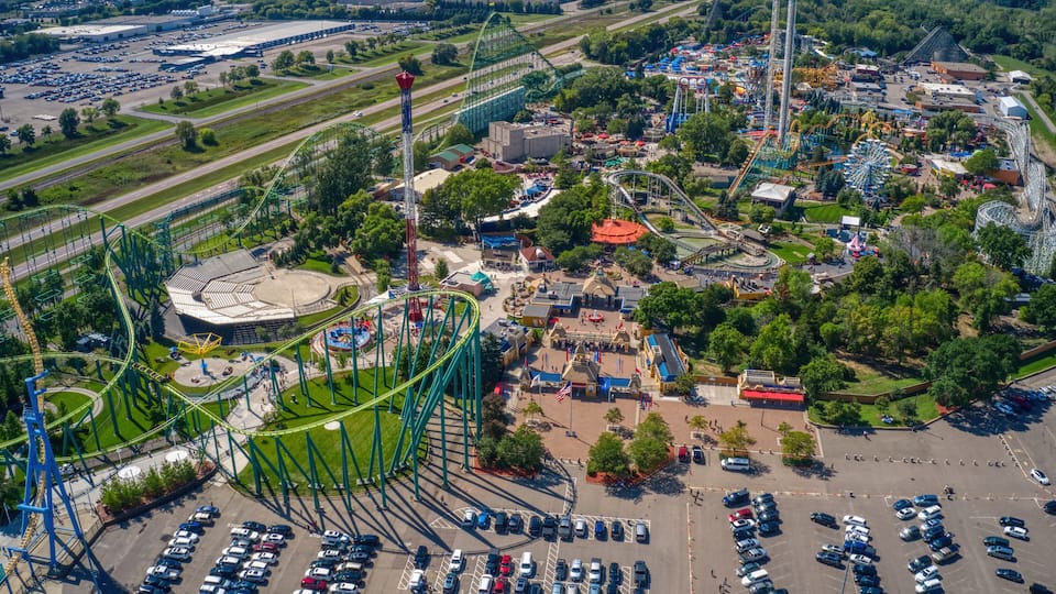 An aerial view of a theme park with roller coasters, a Ferris wheel, and a parking lot.