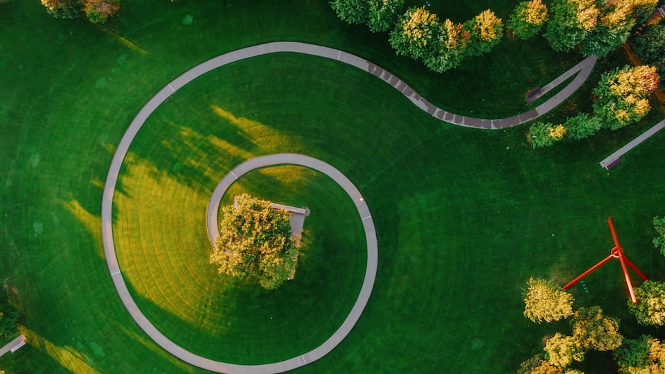 An aerial view of a park with a circular pathway, trees, and a small central area.