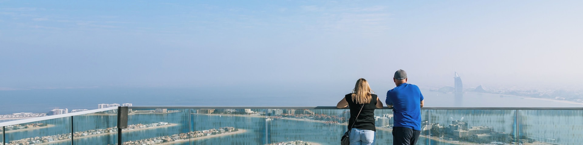 Um casal em uma varanda com vista para uma paisagem costeira urbana, sob um céu limpo.