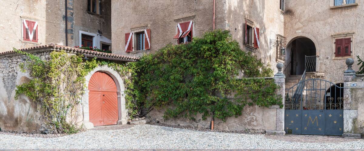A historic building with red shutters, a large arched door, and a gate with a decorative emblem.