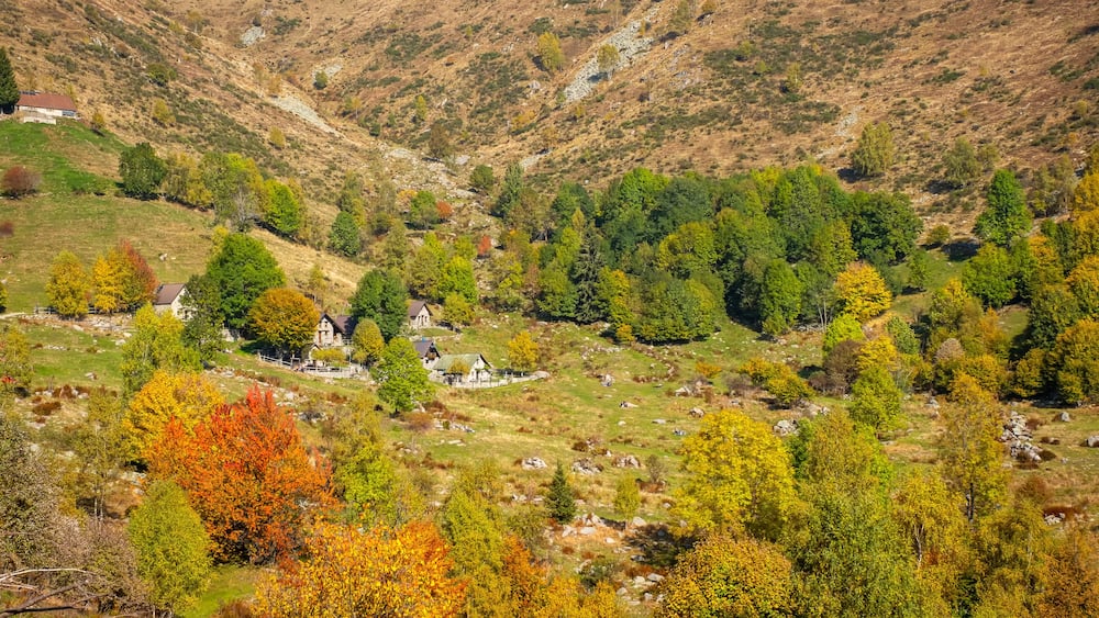 A valley with a small village surrounded by hills and autumn-colored trees.