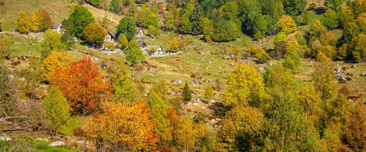 A valley with a small village surrounded by hills and autumn-colored trees.