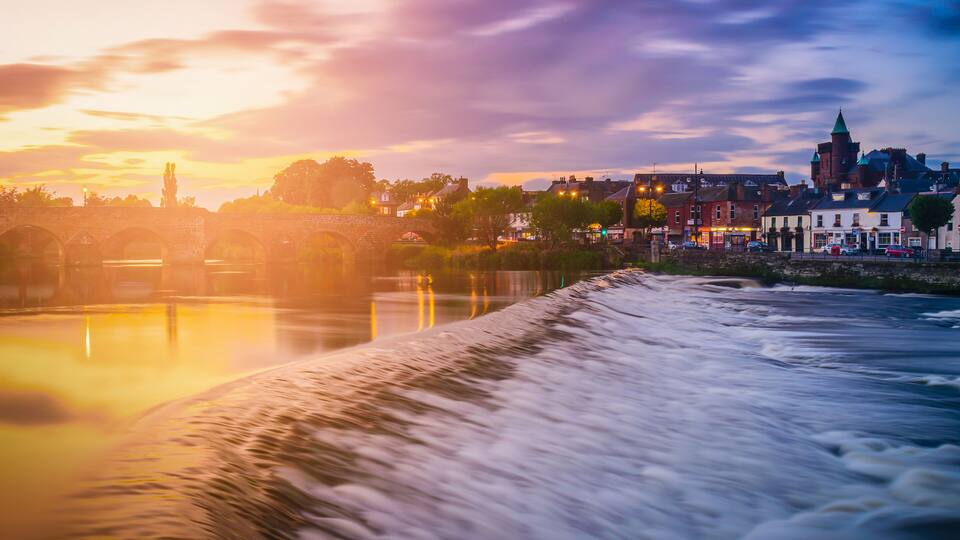 A river with a bridge, a town with historic buildings, and a church tower.