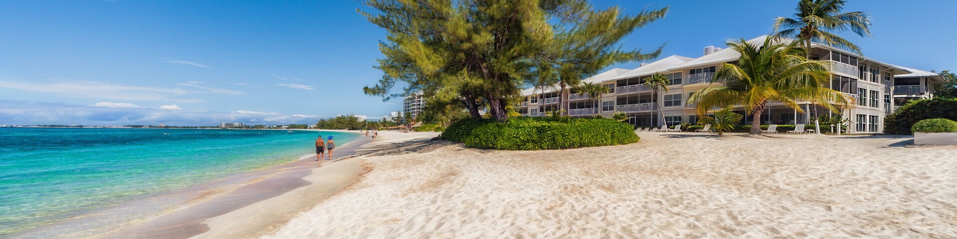 Uma praia com areia branca, águas turquesa cristalinas e um edifício de resort com varandas.