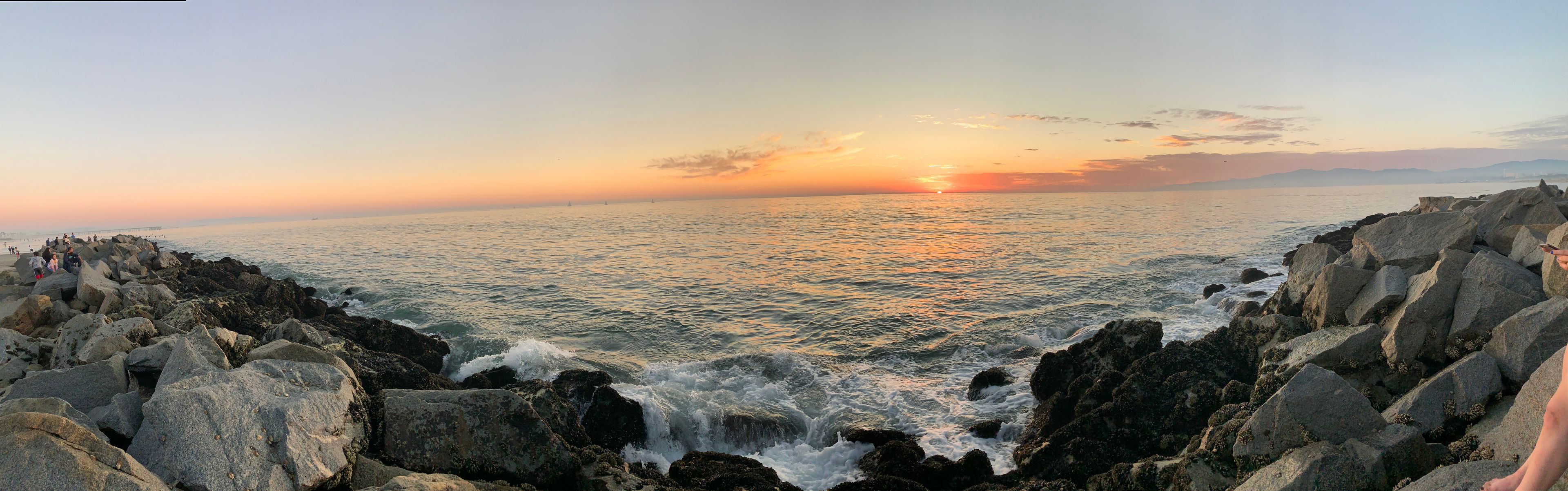 A rocky coastline with waves crashing against the rocks during sunset.