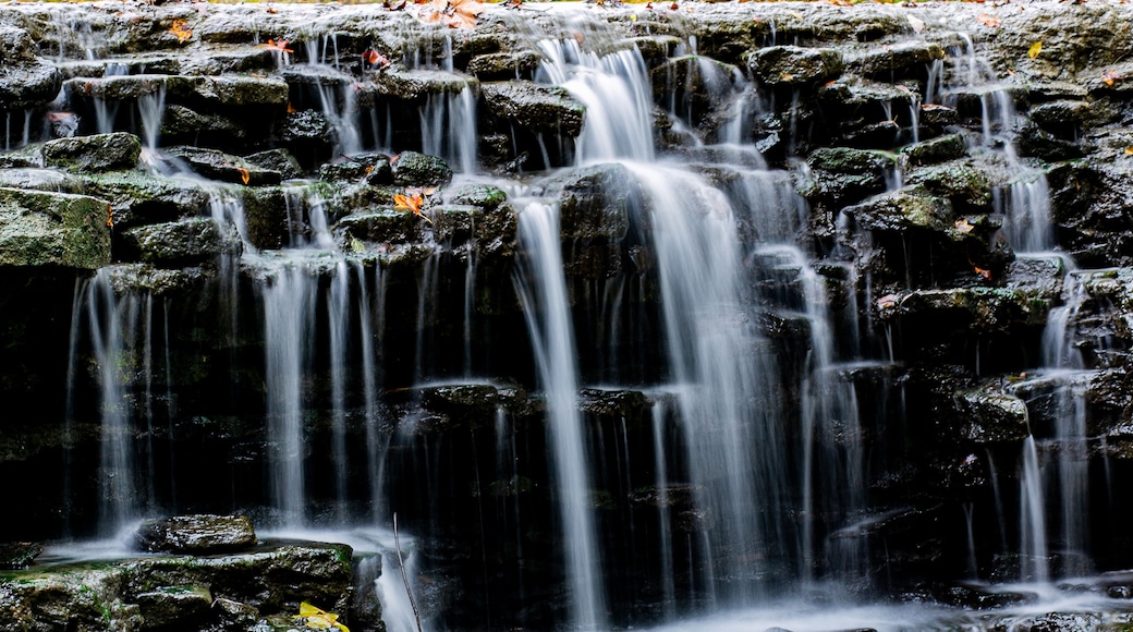 View of water cascading down a tiered rock formation with vibrant autumn foliage above, creating a serene scene, Sharonville, Ohio, United States.