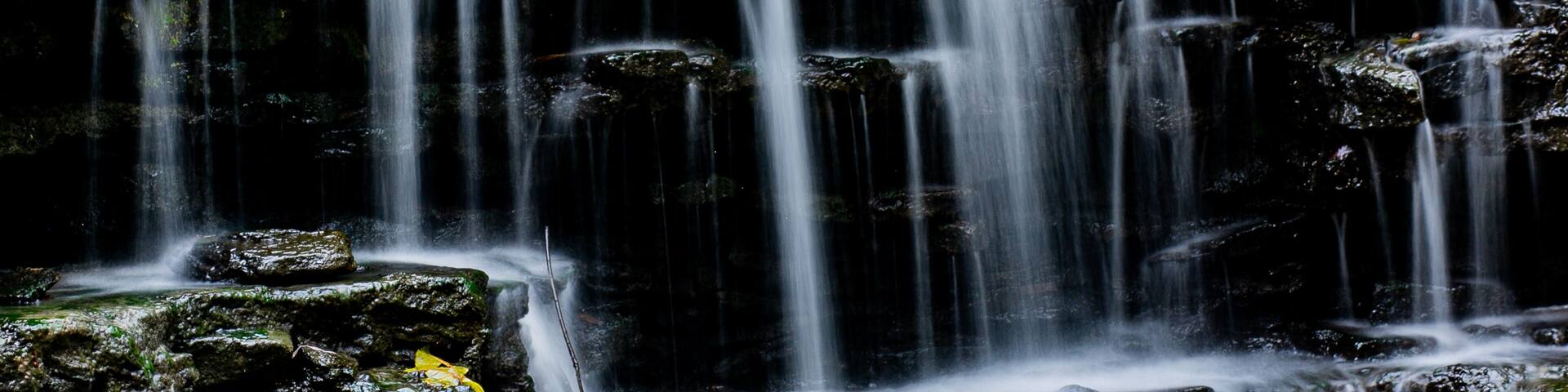 View of water cascading down a tiered rock formation with vibrant autumn foliage above, creating a serene scene, Sharonville, Ohio, United States.