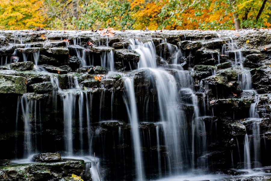 View of water cascading down a tiered rock formation with vibrant autumn foliage above, creating a serene scene, Sharonville, Ohio, United States.