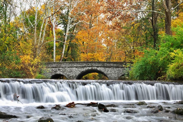 A stone bridge over a waterfall surrounded by autumn foliage.