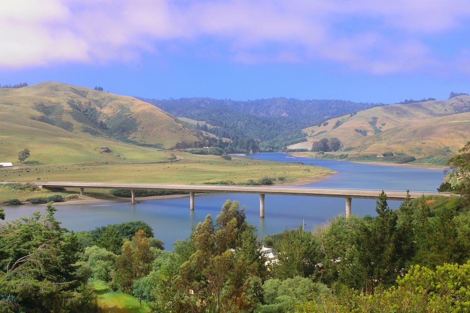 A river with a bridge, surrounded by green hills and trees.