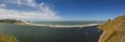 Een kustlandschap met een zandstrand, een rustige zee en rotsachtige kliffen.