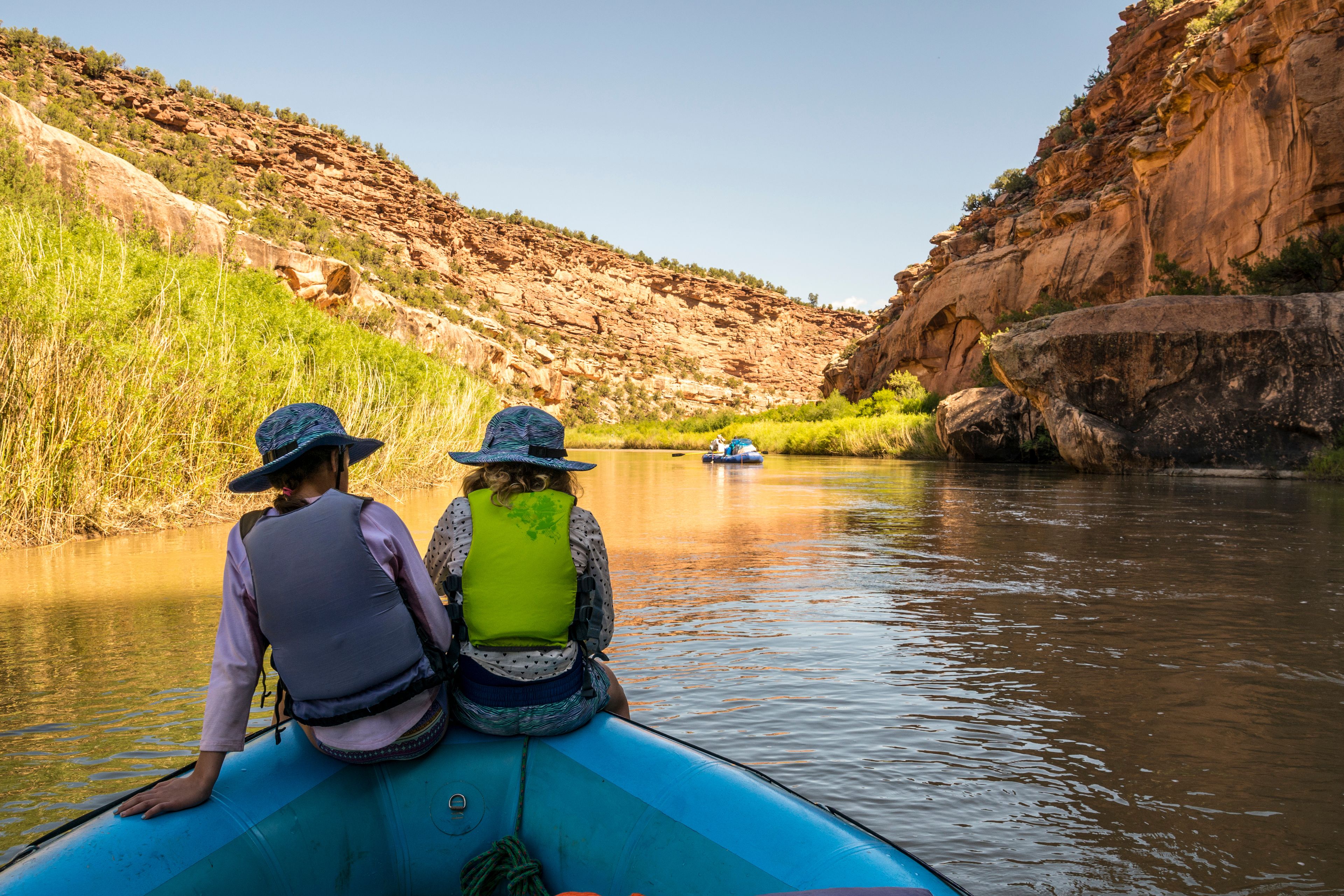 Two people in a blue kayak on a river with a rocky canyon in the background.
