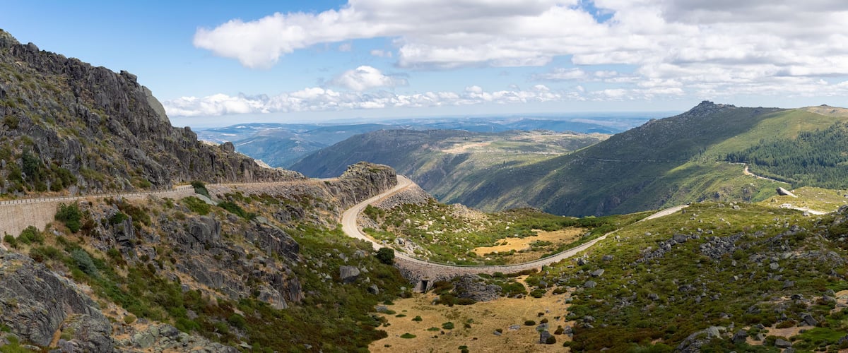 A winding mountain road through a valley with rocky terrain and sparse vegetation.