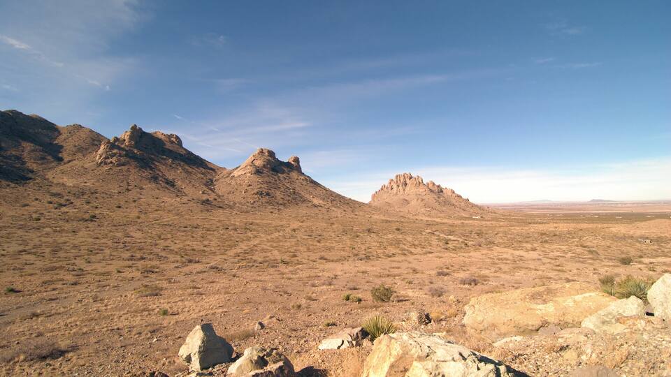 A desert landscape with rocky terrain and distant mountains under a clear sky.
