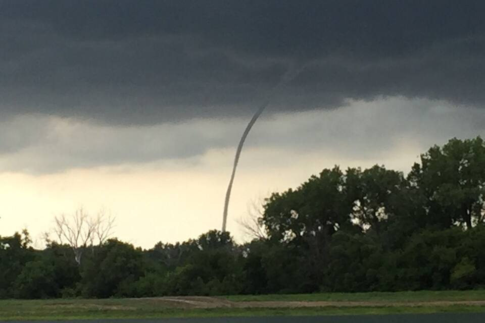A tornado touching down near a body of water with trees in the background.